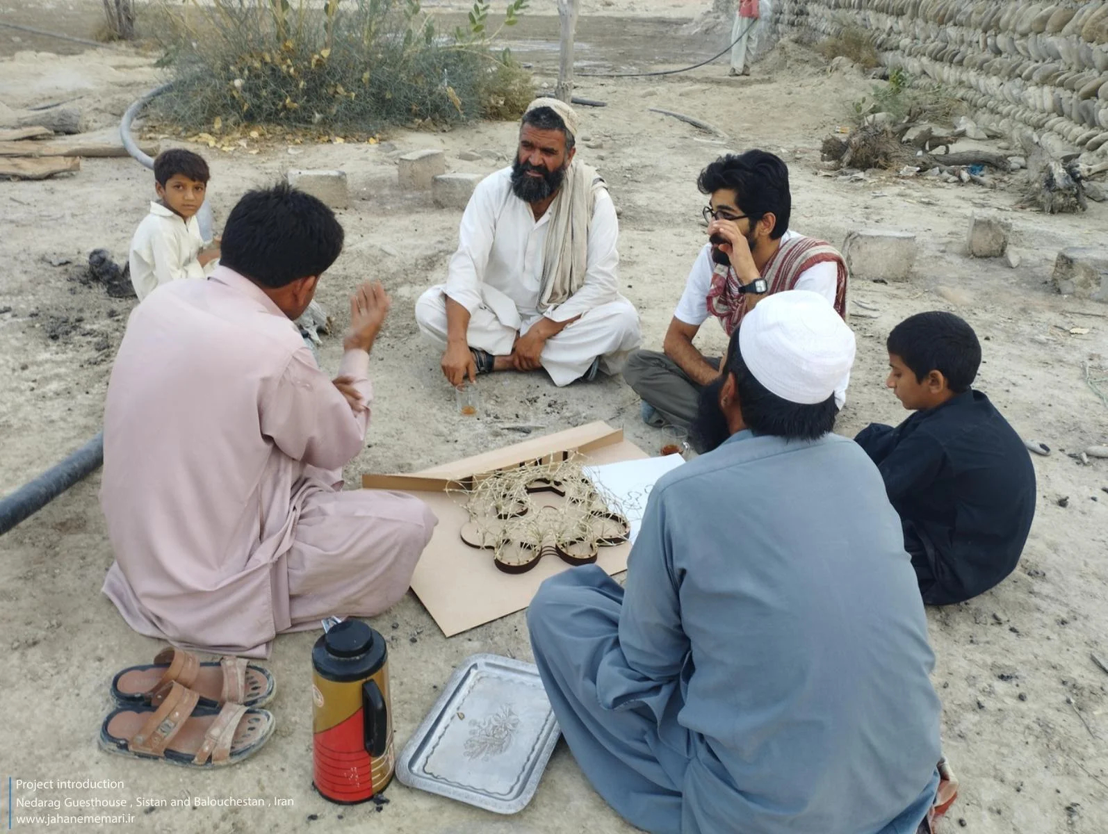 نمای خارجی و داخلی مهمانسرای ندارگ در روستای کهنانیکش، سیستان و بلوچستان، که ساختار نیمه‌باز، سقف چتری‌شکل با خرپاهای دست‌ساز و دیوارهای ضخیم گلی آن بر اساس بازتفسیر معماری بومی «کپر» و با هدف خنک‌سازی طبیعی و مشارکت جمعی اهالی طراحی و اجرا شده است.